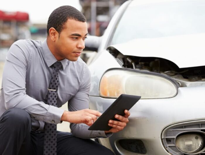 An insurance adjuster examines a damaged car and inputs data into a tablet while in the field using XactAnalysis.