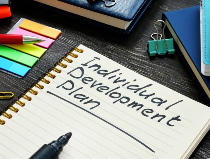 Individual development plan words written on paper sitting on a wooden surface with colored Post-it notes next to it.