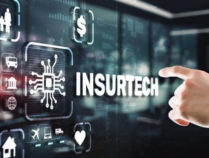 A person wearing a suit extends a finger toward a computer screen to touch the word insurtech.