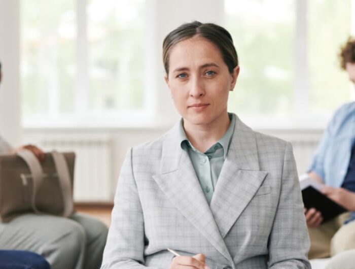 Female insurance adjuster holding a clipboard in front of a couple seated in chairs.